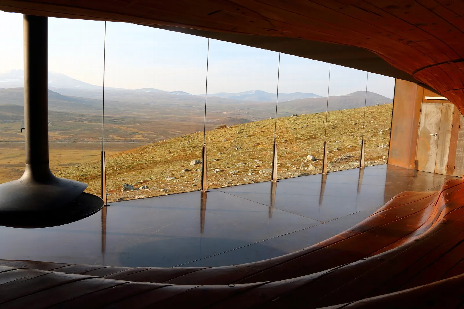 The curved timber interior of Viewpoint Snøhetta framing the Dovrefjell landscape through its glass wall